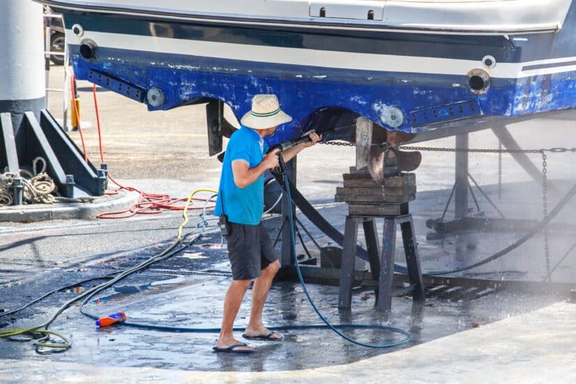 Person Cleaning Underneath A Boat With A Pressure Device